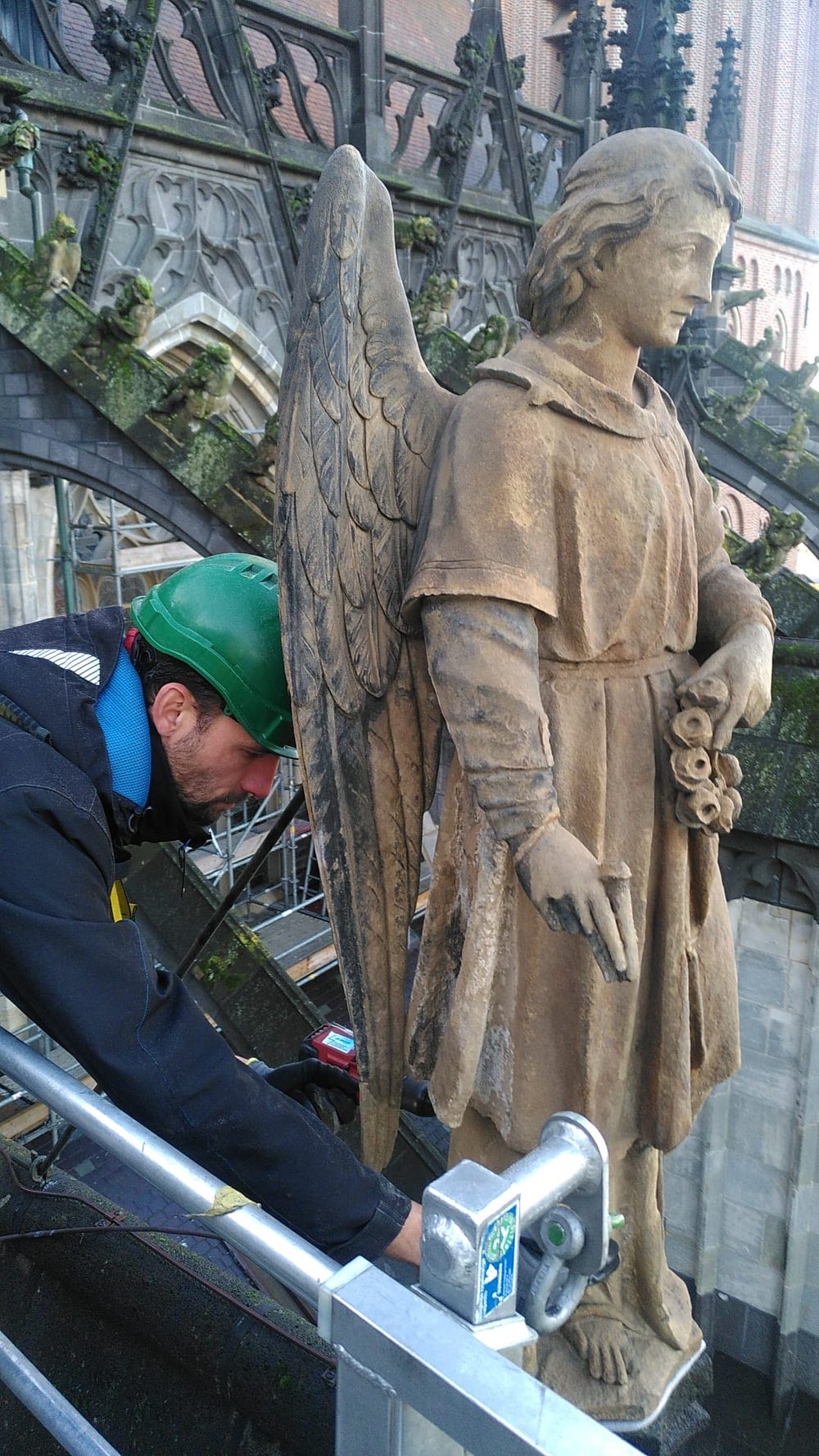 Martijn de Bruijn aan het werk op het dak van de Sint-Janskathedraal, naast een stenen engelbeeld